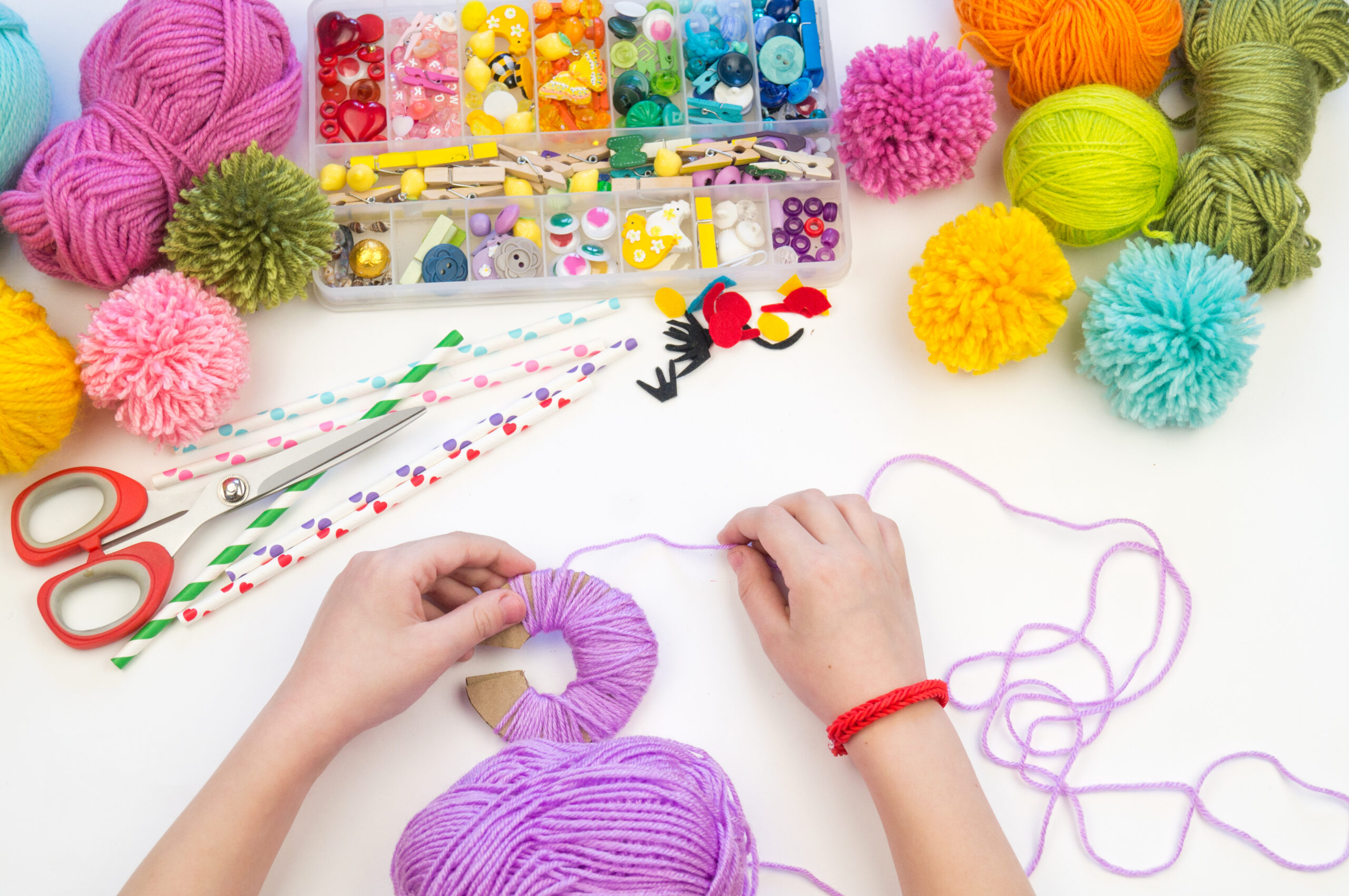 The child is engaged in a favorite hobby. The kid makes a pom-pom from a woolen thread monster. Holiday toy gift.